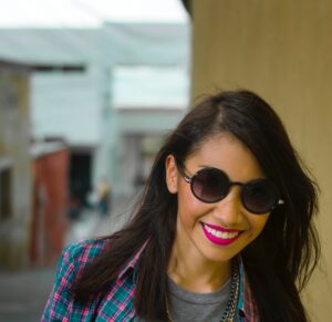 A young woman smiling while wearing sunglasses with diminished jaw pain from TMJ treatment.