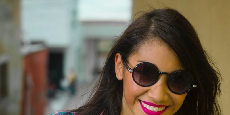 A young woman smiling while wearing sunglasses with diminished jaw pain from TMJ treatment.