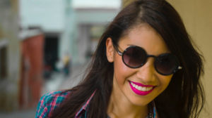 A young woman smiling in sunglasses after same-day dental crowns in Oceanside.