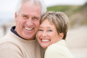An older man and woman smiling together on the beach after restorative dentistry in Oceanside.