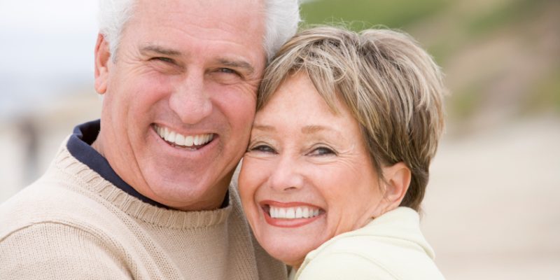 An older man and woman smiling together on the beach after restorative dentistry in Oceanside.